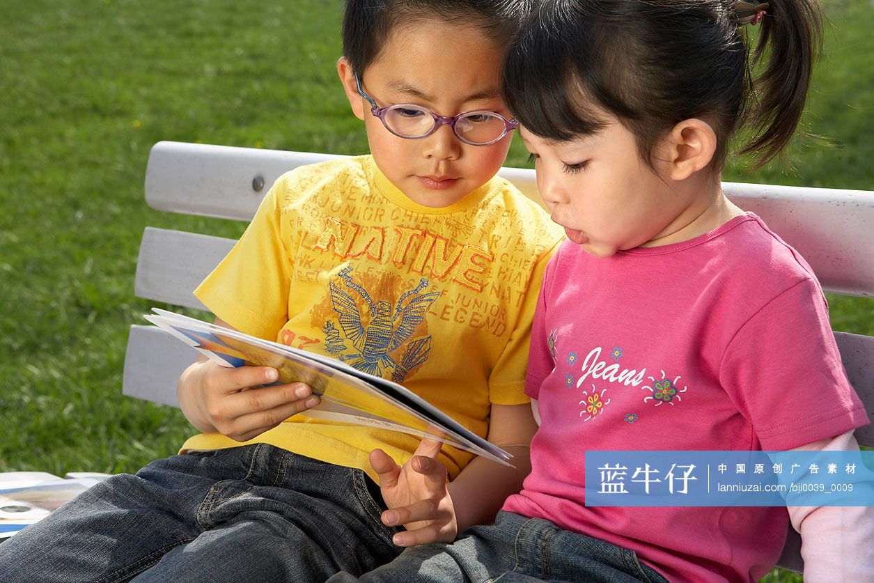 小男孩和小女孩在公园长椅上看卡片