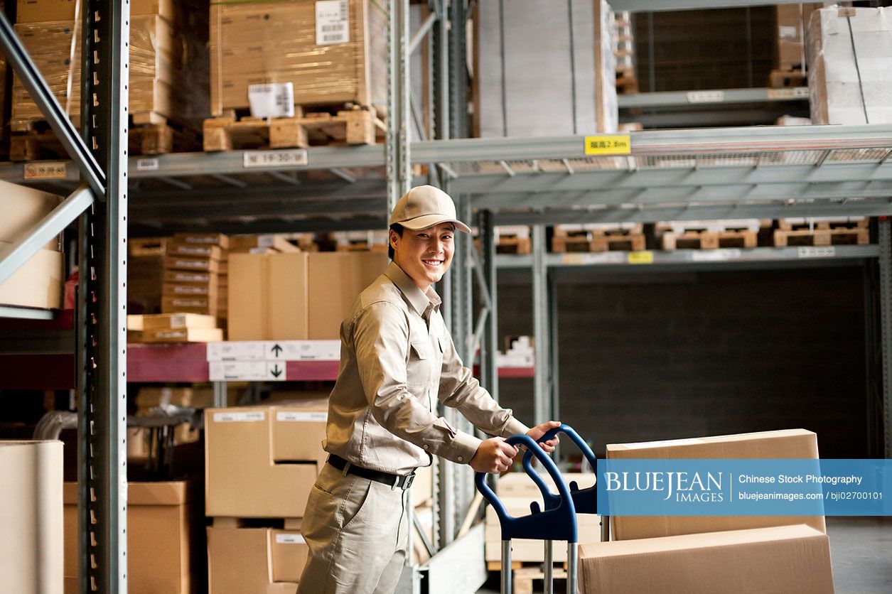Male Chinese warehouse worker pushing boxes