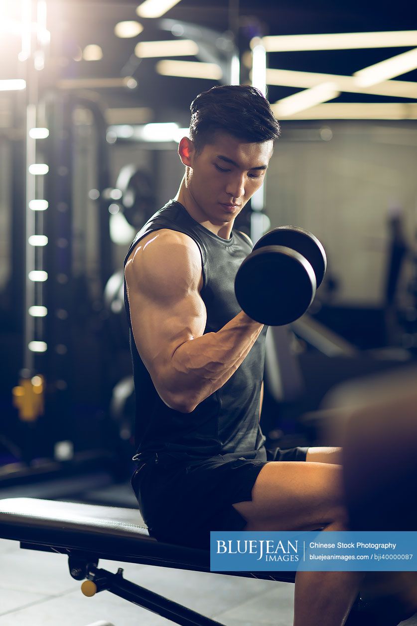 Young Chinese man working out with dumbbell at gym