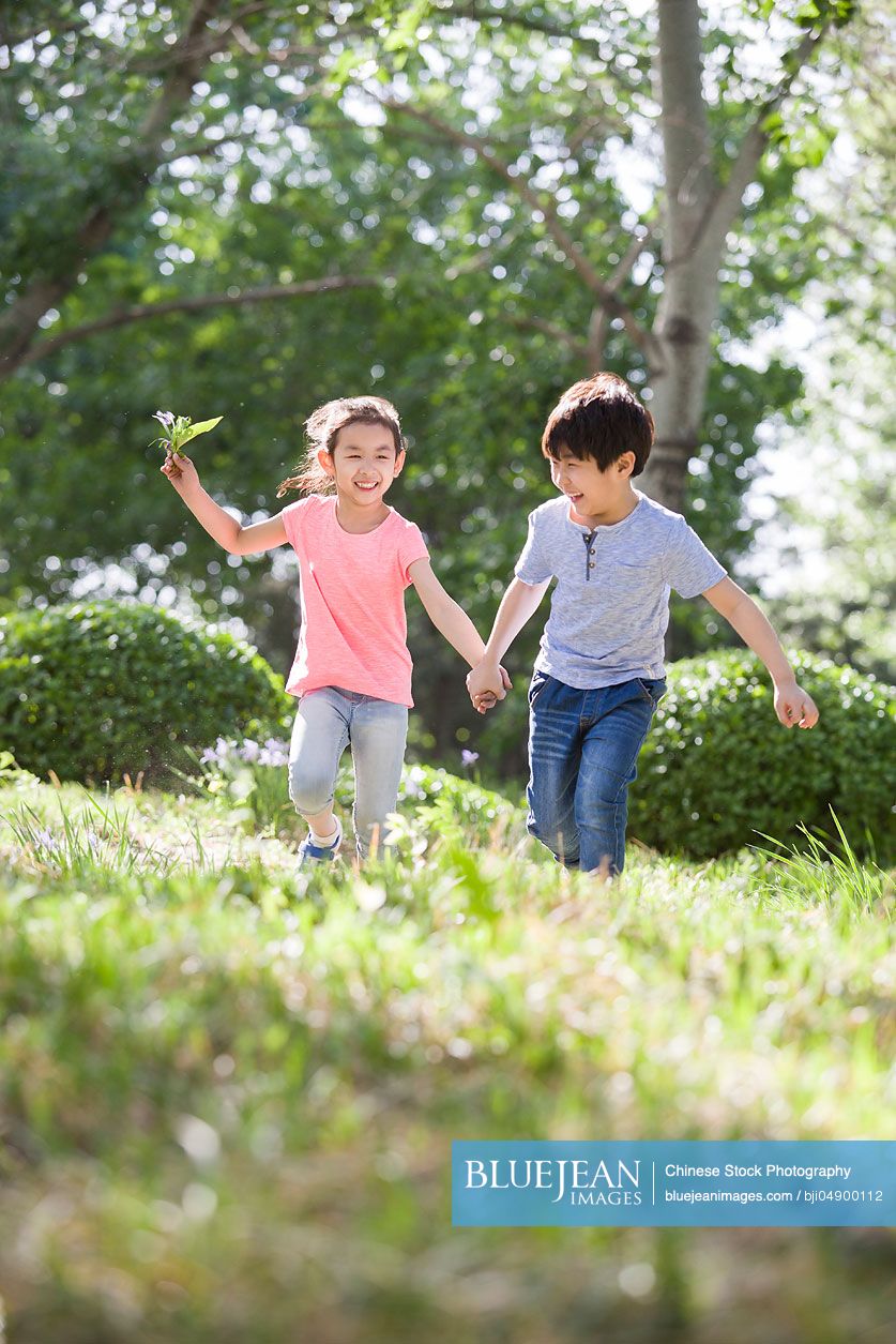 Happy Chinese children holding hands running in woods