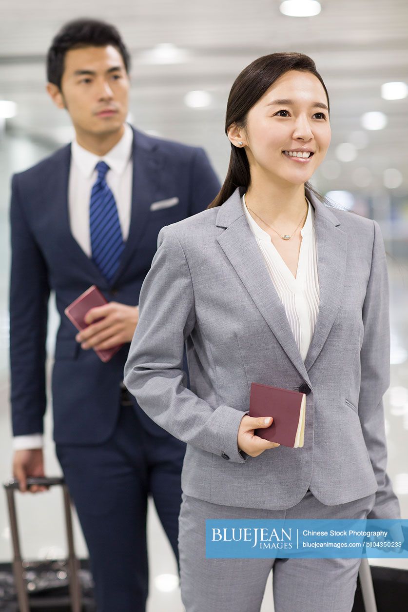 Young Chinese business person walking in airport with suitcases