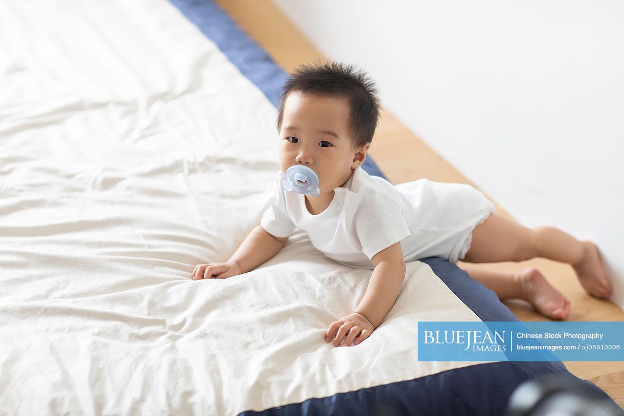 Cute Chinese baby lying on bed with pacifier