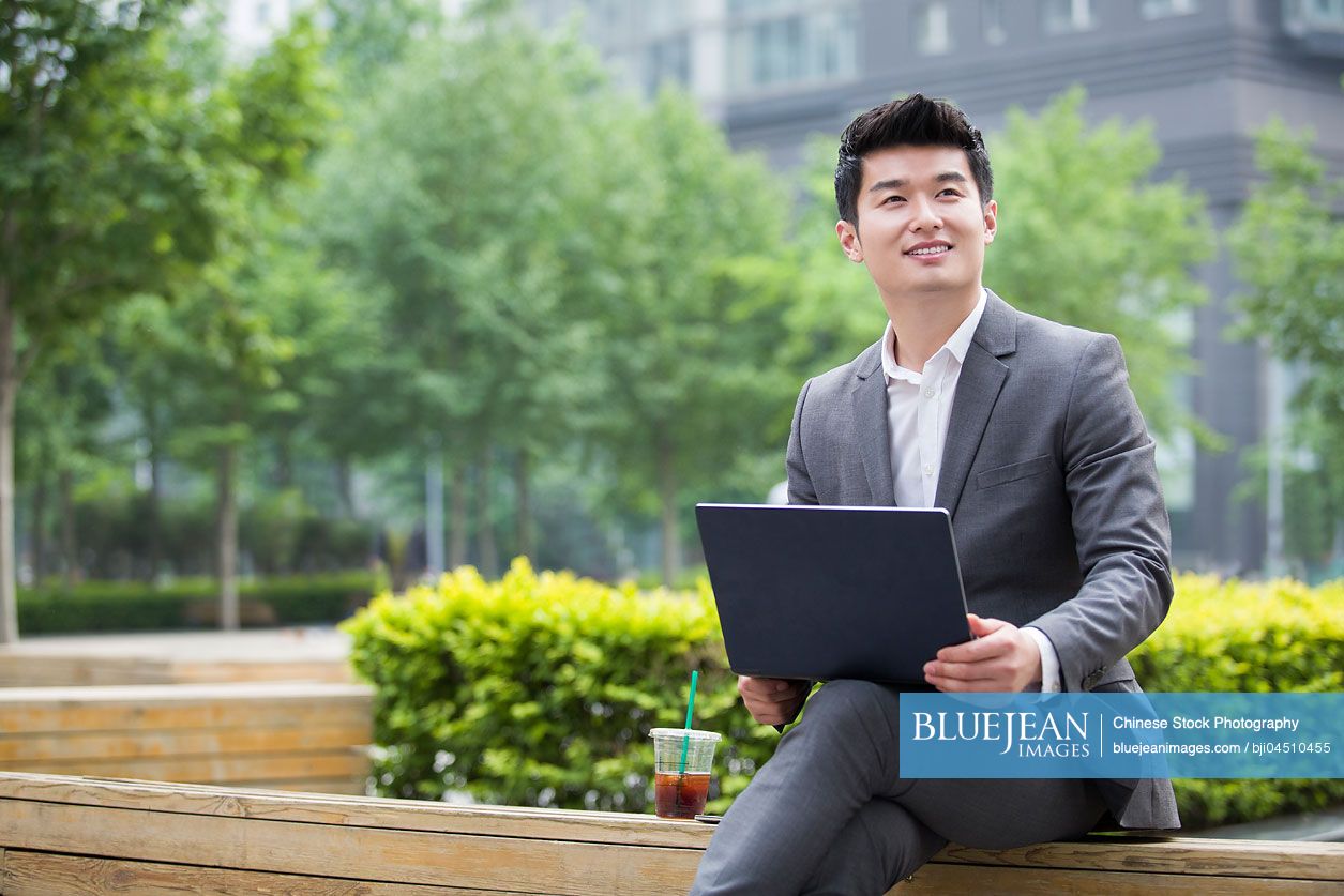Young Chinese businessman working with laptop outdoors
