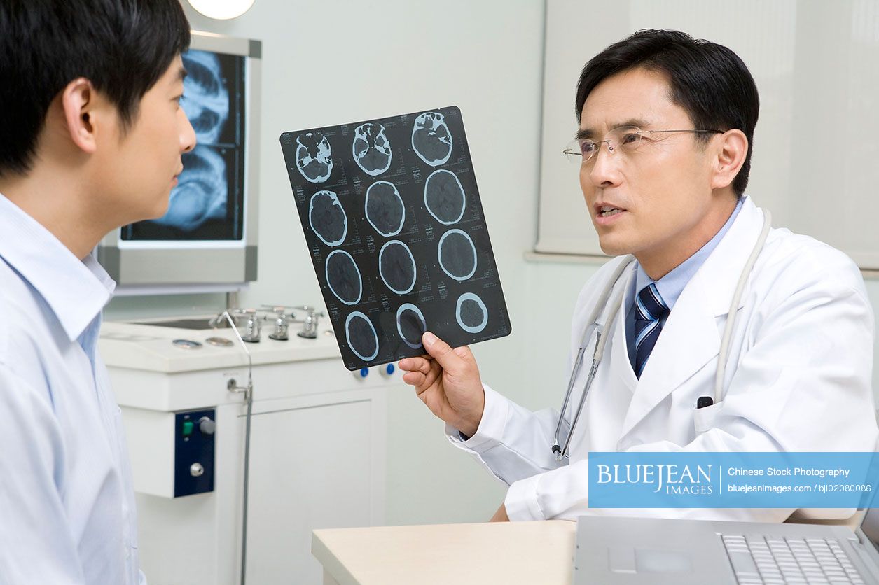 Male Chinese doctor analyzing X-ray plate with patient