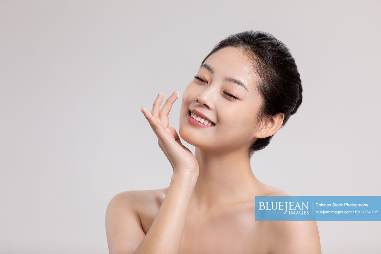 Beautiful young Chinese woman applying moisturizer