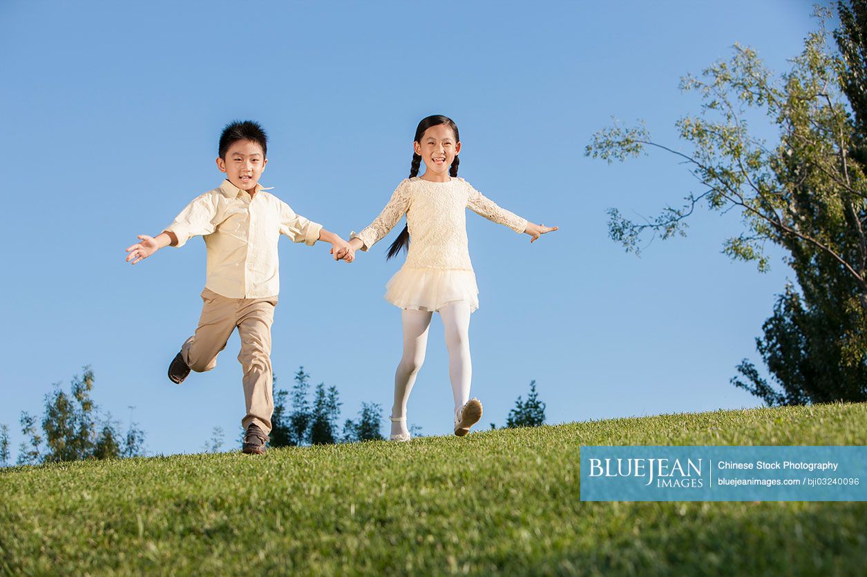 Chinese little girl and boy pretending to be flying in a park