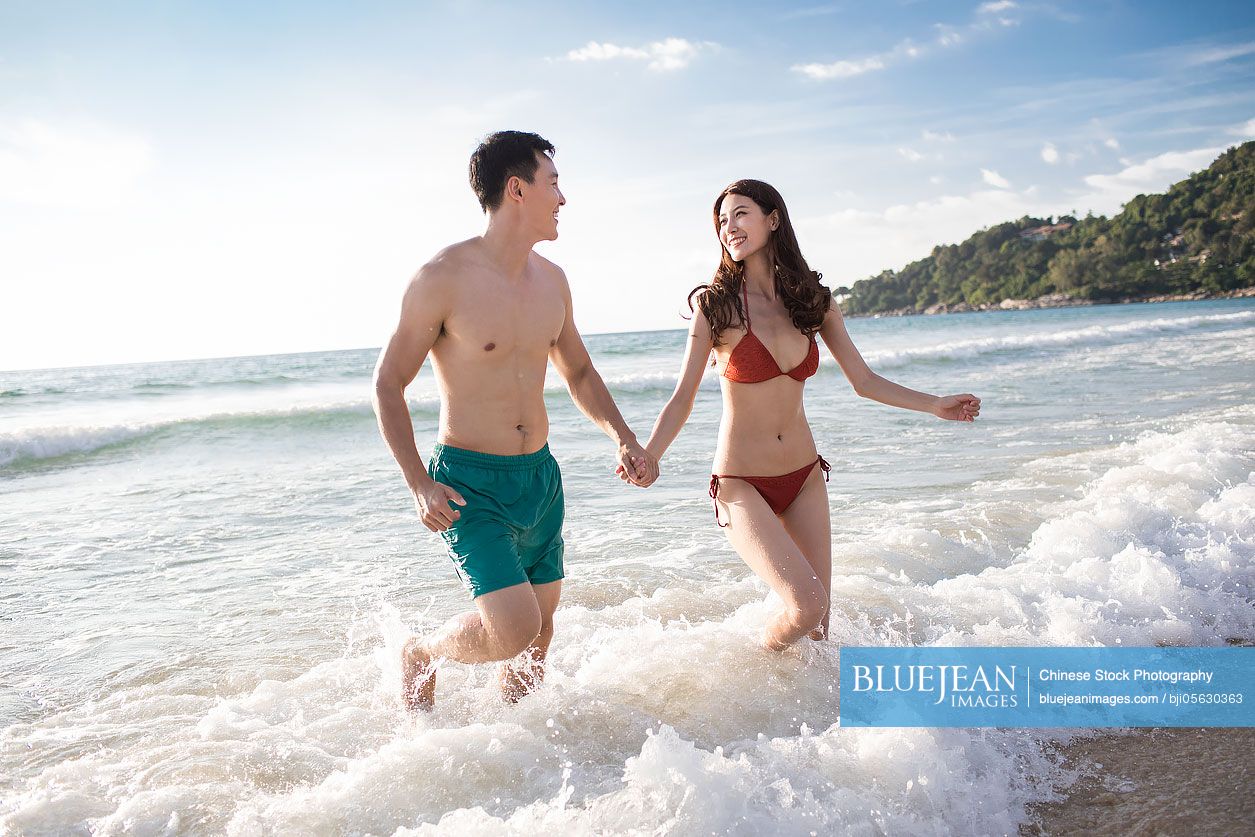 Happy young Chinese couple running in sea water