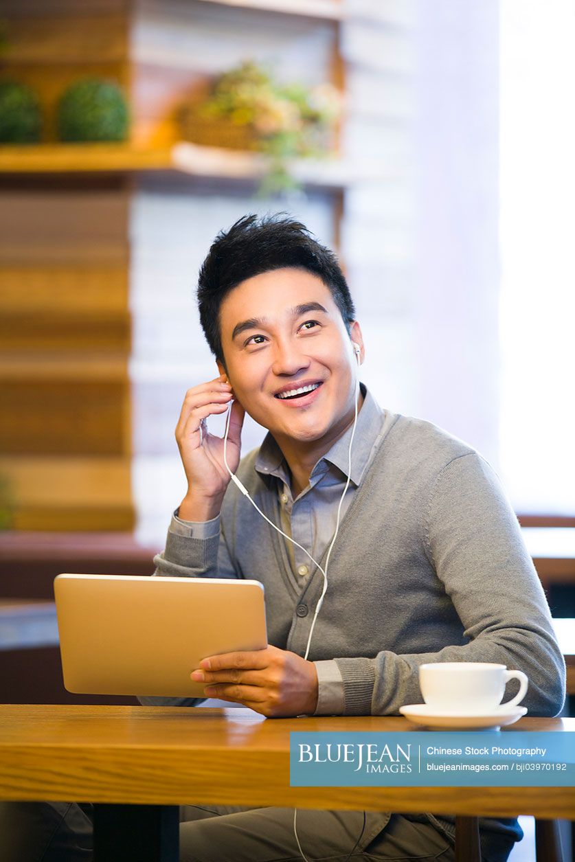 Young Chinese man enjoying music in digital tablet in coffee shop