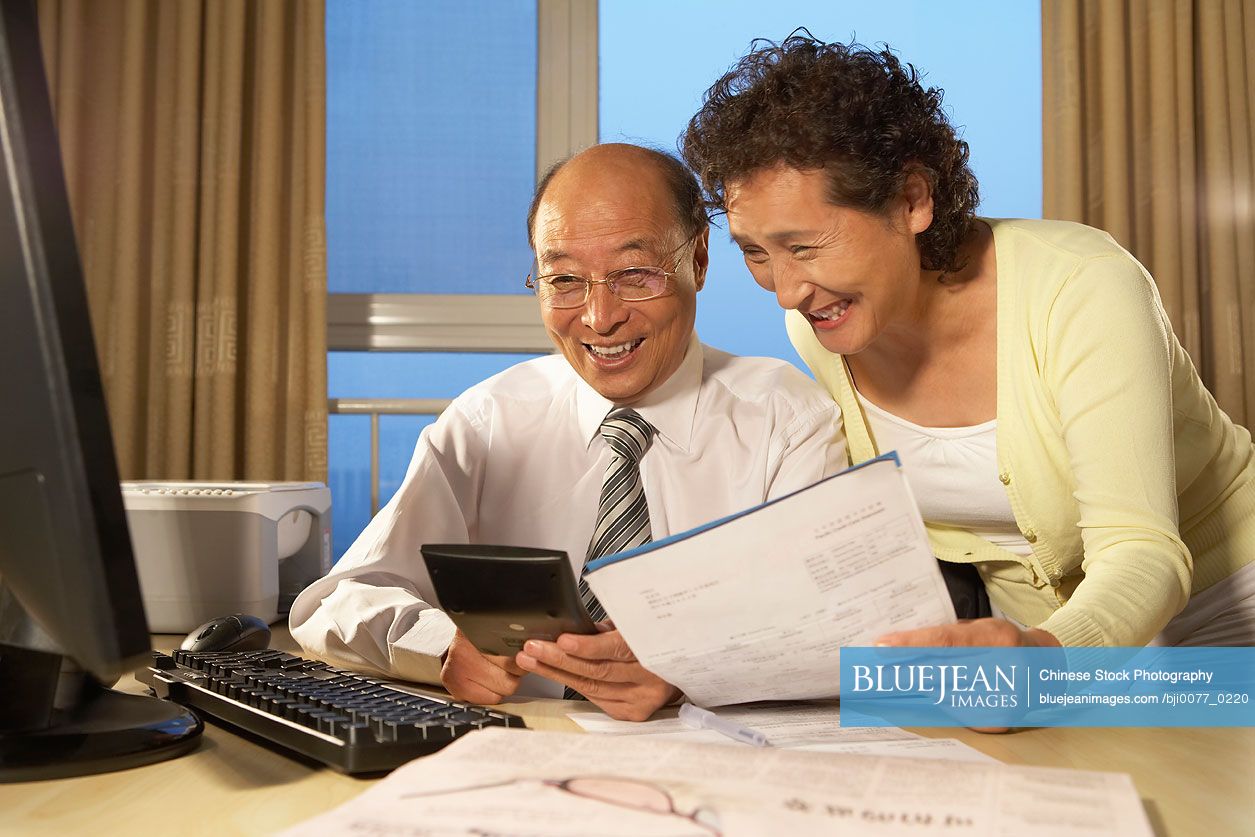 Chinese Businessman And Business Chinese Woman Smiling, Looking At Calculator