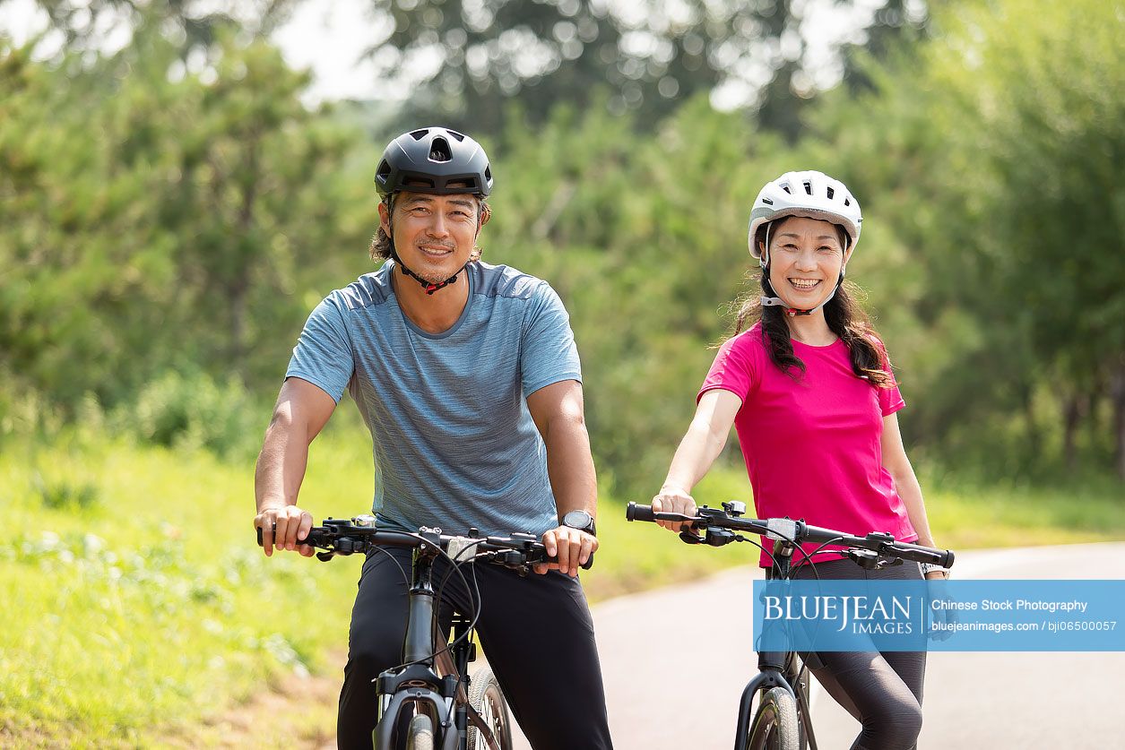 Happy mature Chinese couple riding bikes in park