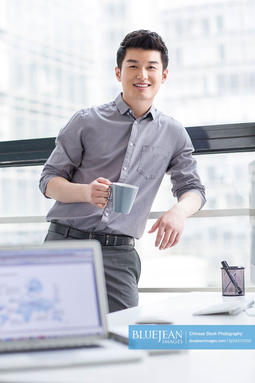 Young Chinese businessman drinking coffee in office