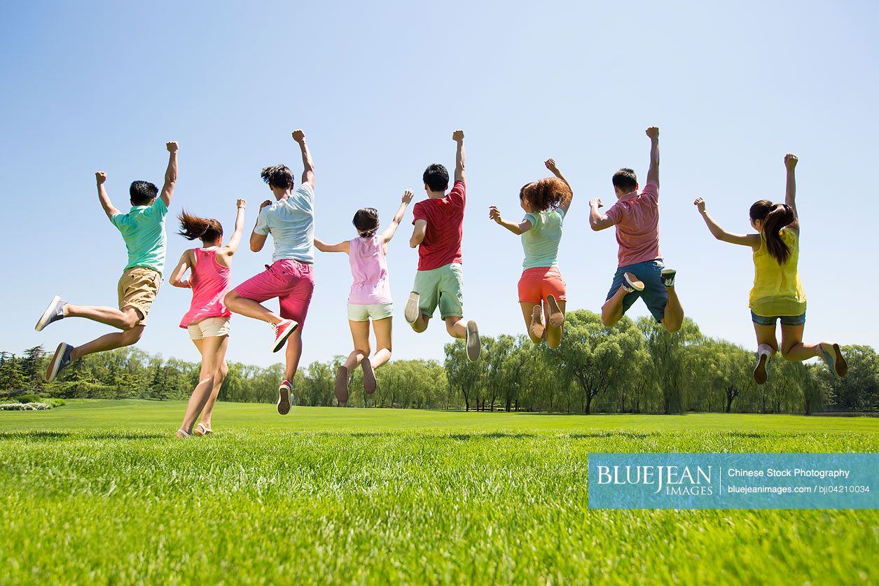 Rear view of eight cheerful young Chinese adults jumping on grass