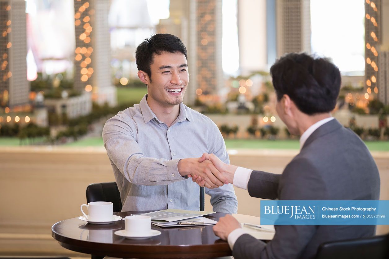 happy-young-chinese-man-buying-new-house-from-realtor-high-res-stock