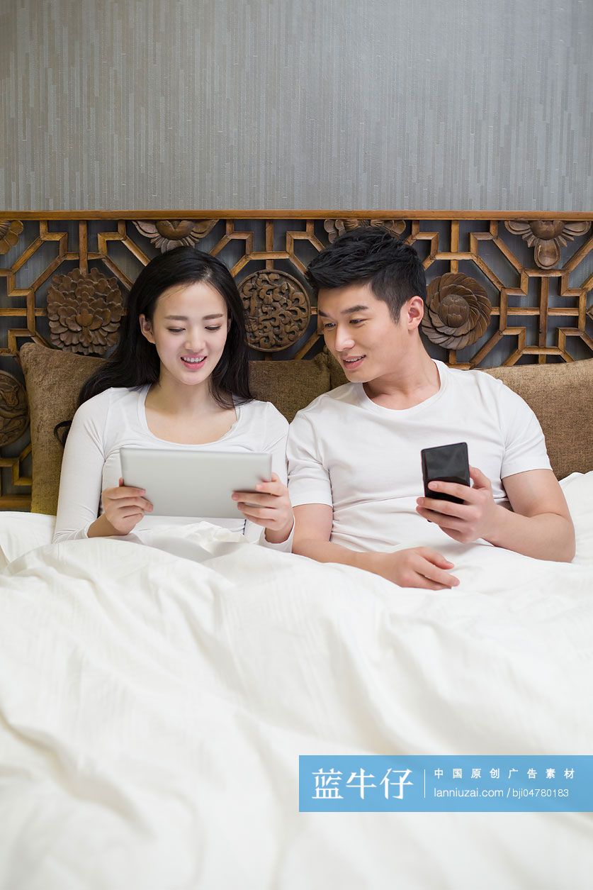年轻夫妻在卧室玩平板电脑和手机