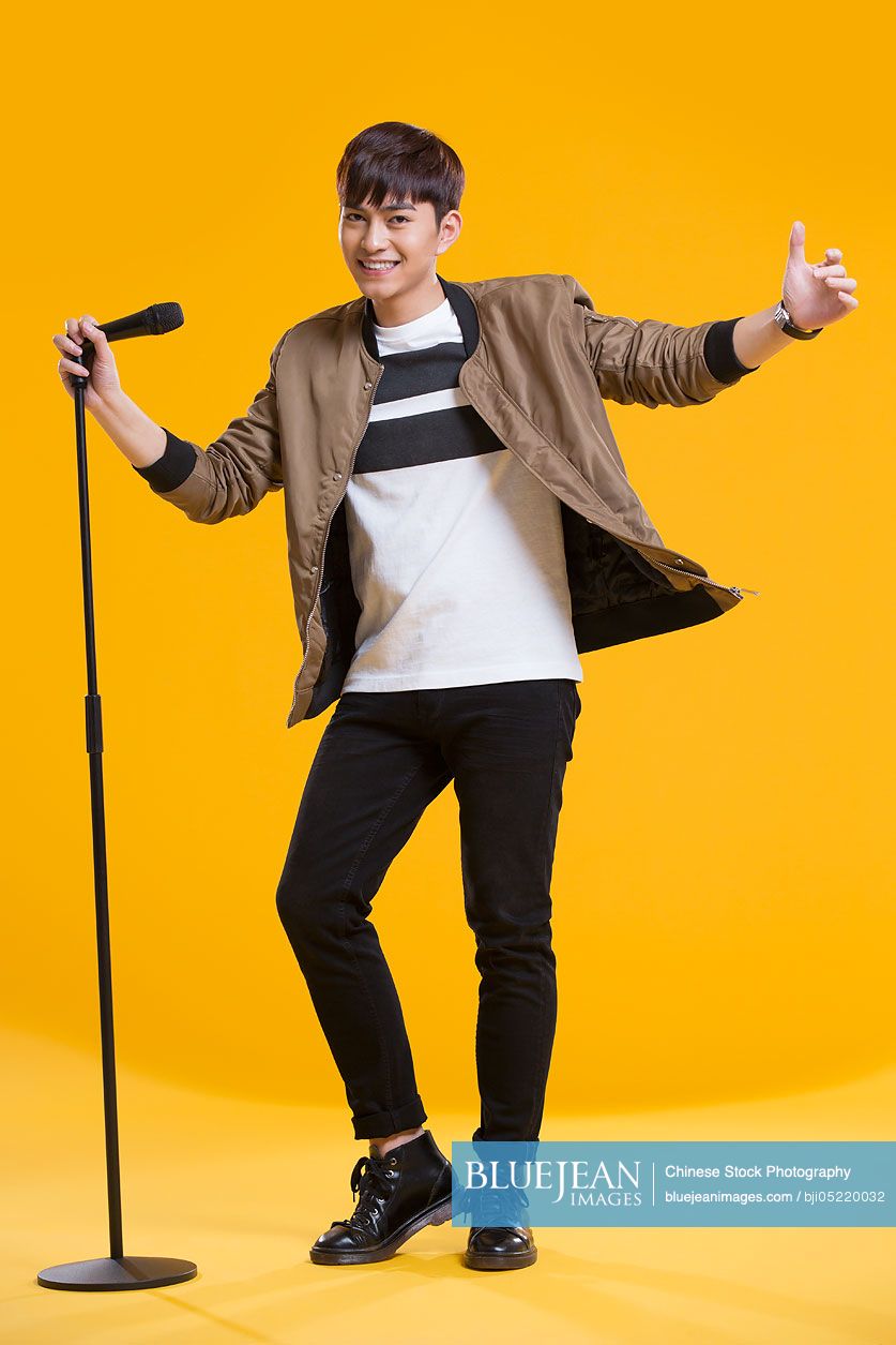 Cheerful young Chinese man singing with microphone