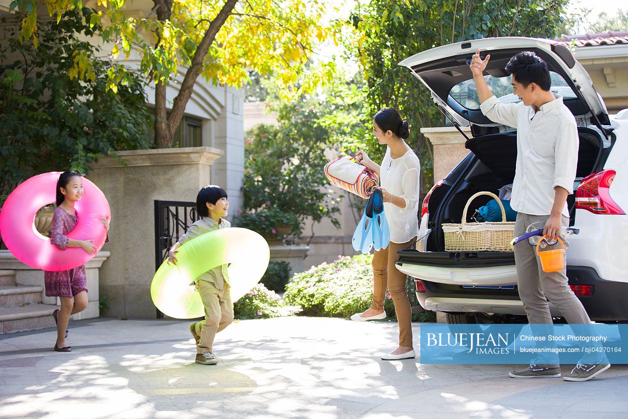 Young Chinese family putting water sports equipment into the car
