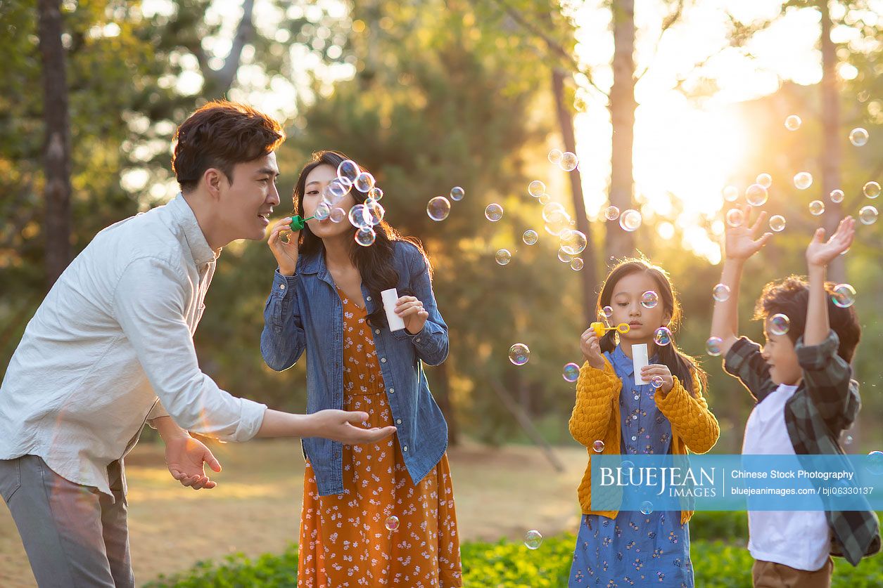 Happy young Chinese family blowing bubbles in park