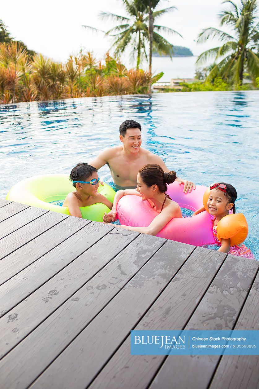 Happy young Chinese family having fun in swimming pool