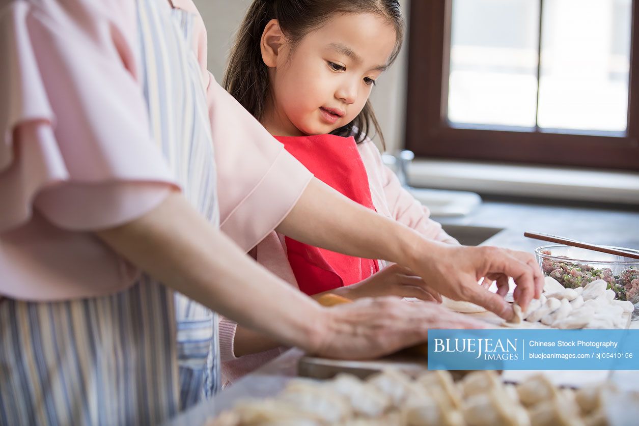 Cheerful Chinese granddaughter and grandmother making dumplings in kitchen