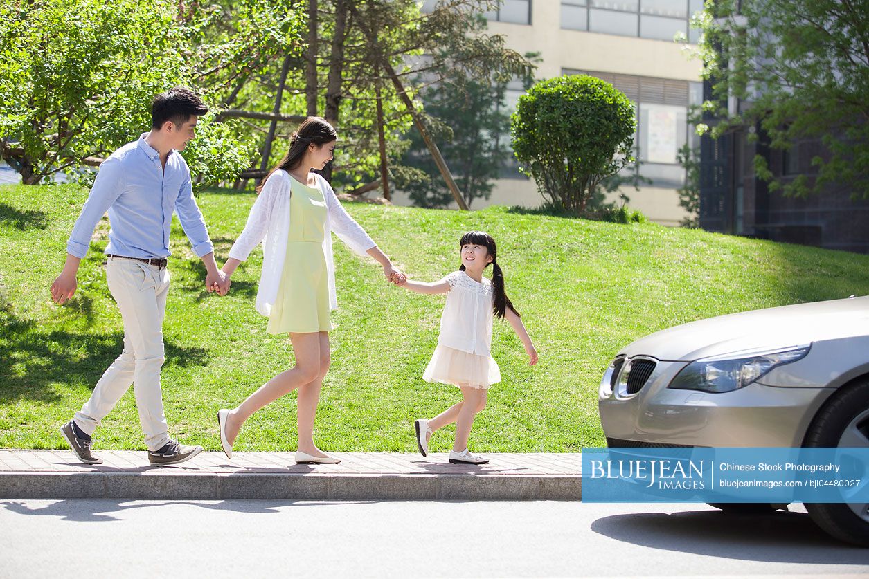 Happy young Chinese family holding hands walking