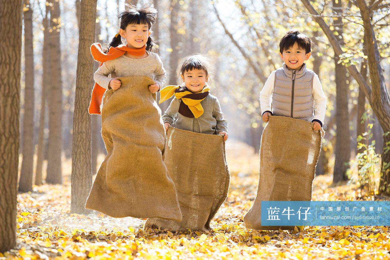 三个小孩在树林里玩布袋赛跑游戏