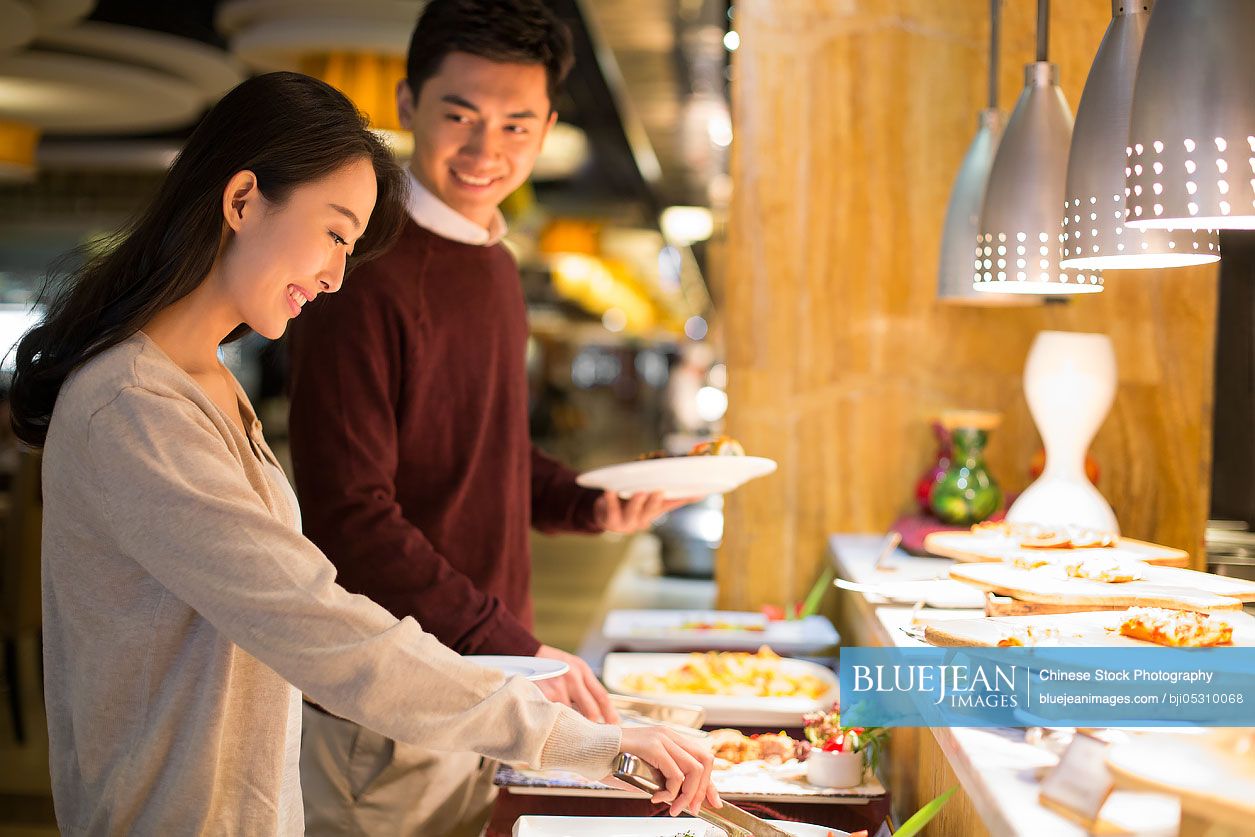 Cheerful young Chinese couple taking food from buffet table