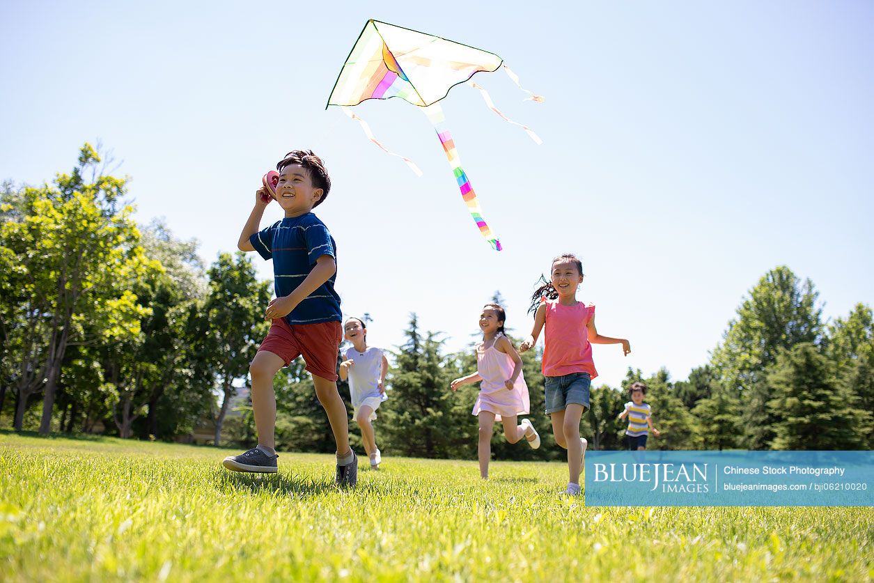 Happy Chinese children running with a kite on meadow