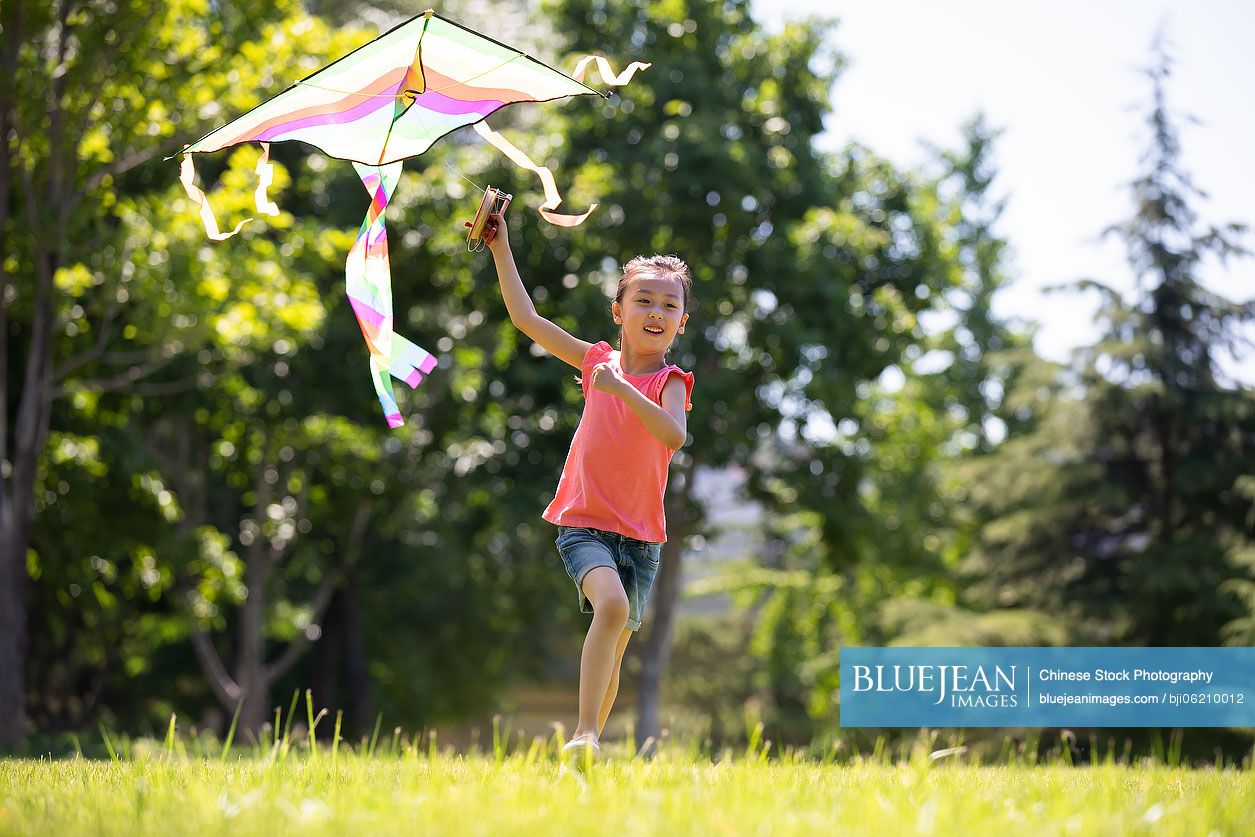 Happy little Chinese girl running with a kite on meadow