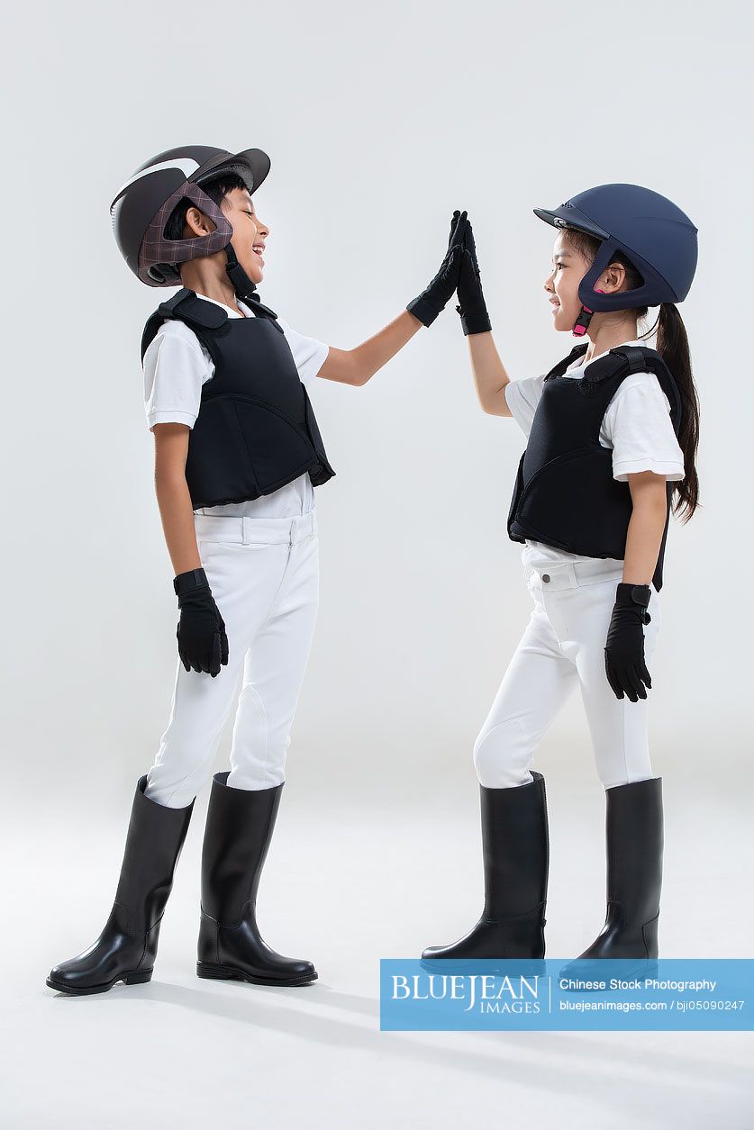 Happy Chinese sibling in riding clothes high fiving