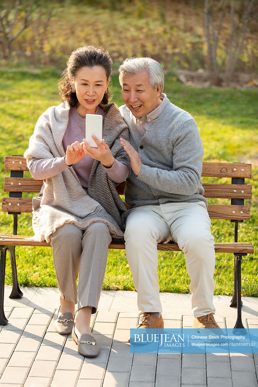 Cheerful senior Chinese couple using smart phone in the park