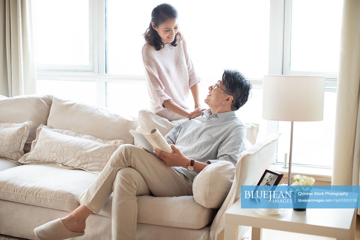 Happy mature Chinese couple reading book in living room