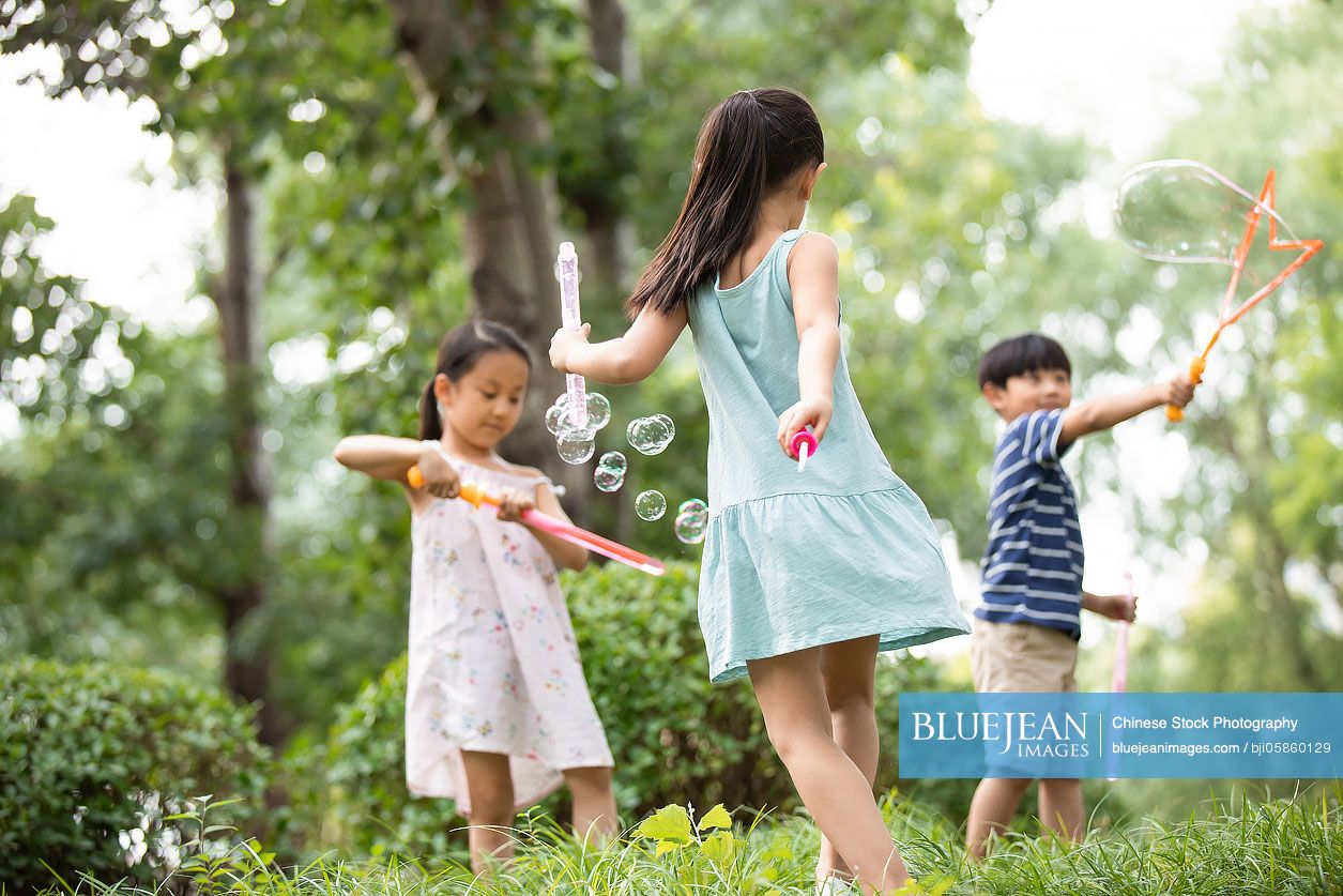 Three Chinese children blowing bubbles on grass
