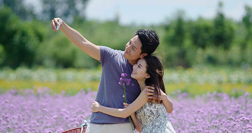 Happy young Chinese couple taking selfie in flower field,4K