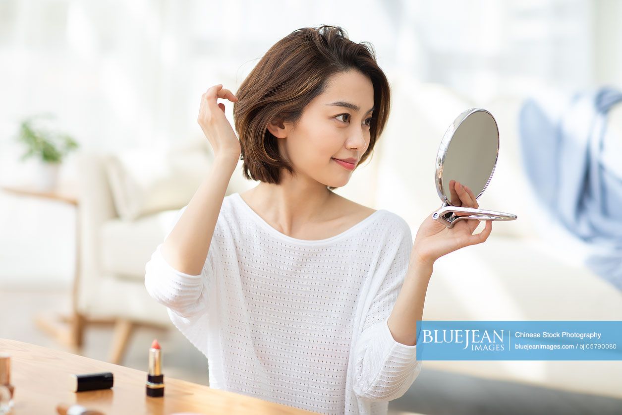 Young Chinese woman applying lipstick at home