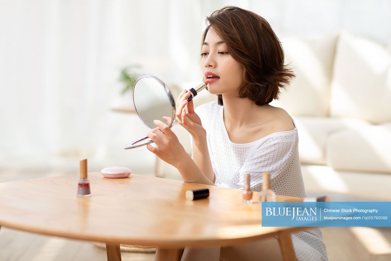 Young Chinese woman applying makeup at home