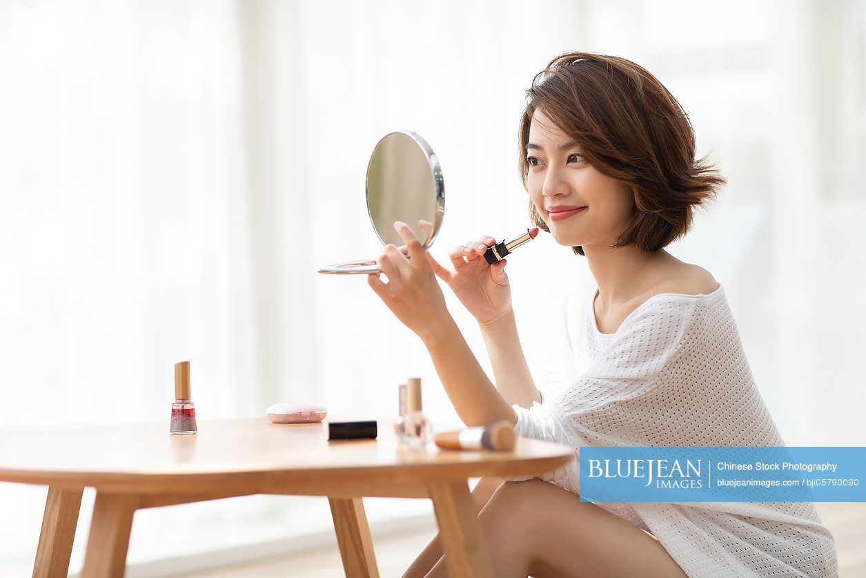 Young Chinese woman applying makeup at home