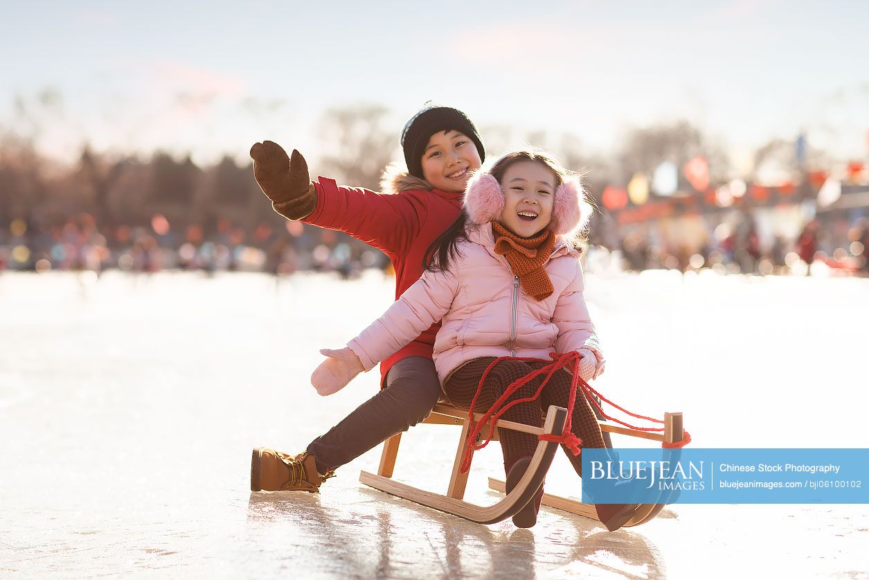 Happy Chinese sibling sledding outdoors