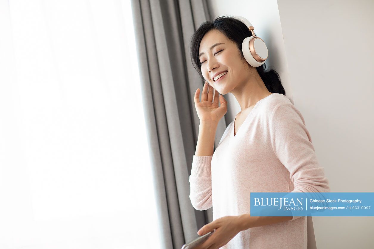 Happy young Chinese woman listening to music in living room