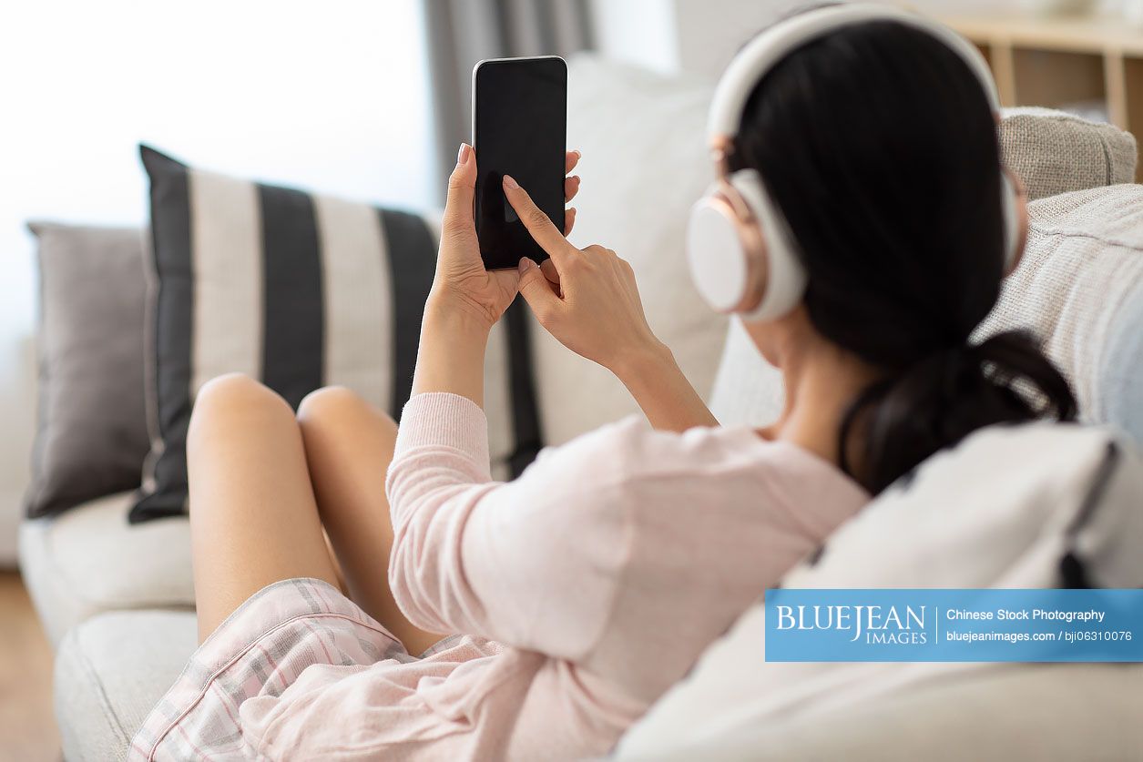 Young Chinese woman using smartphone on sofa