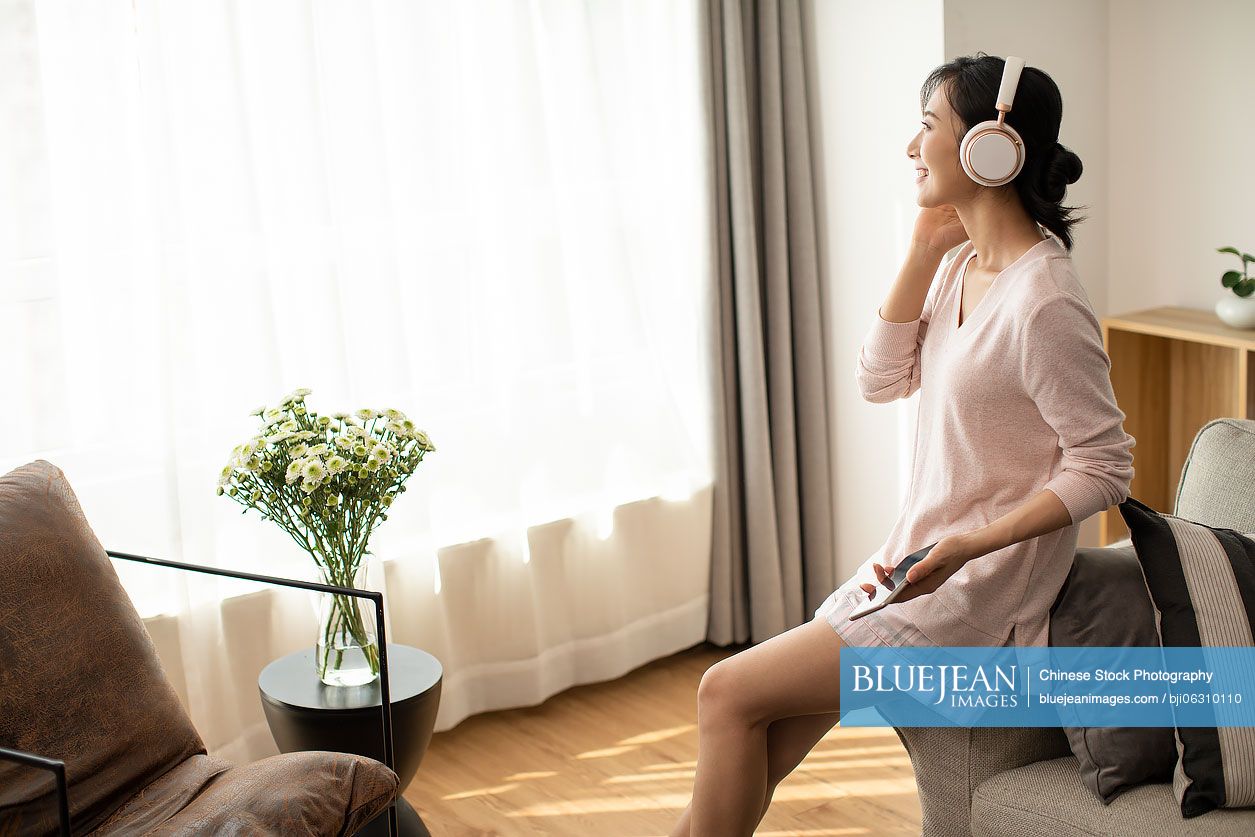 Happy young Chinese woman listening to music in living room