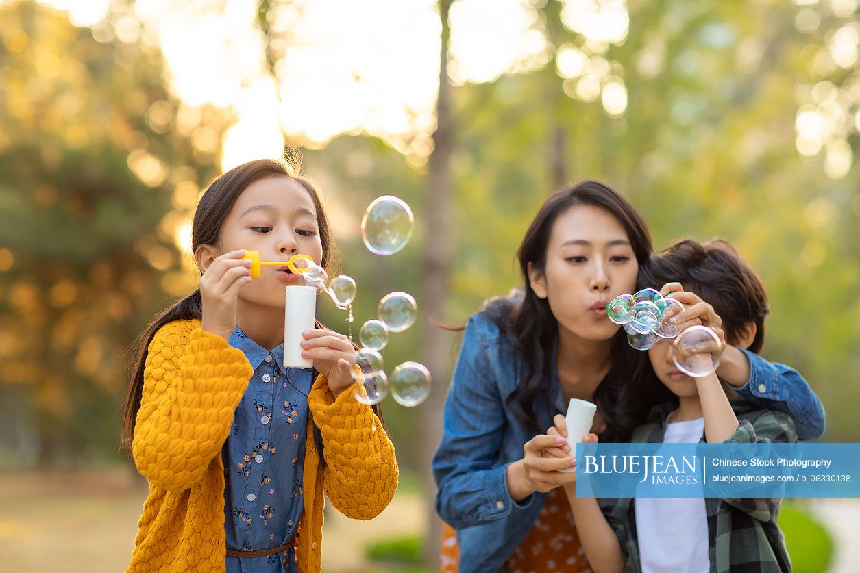 Happy young Chinese family blowing bubbles in park