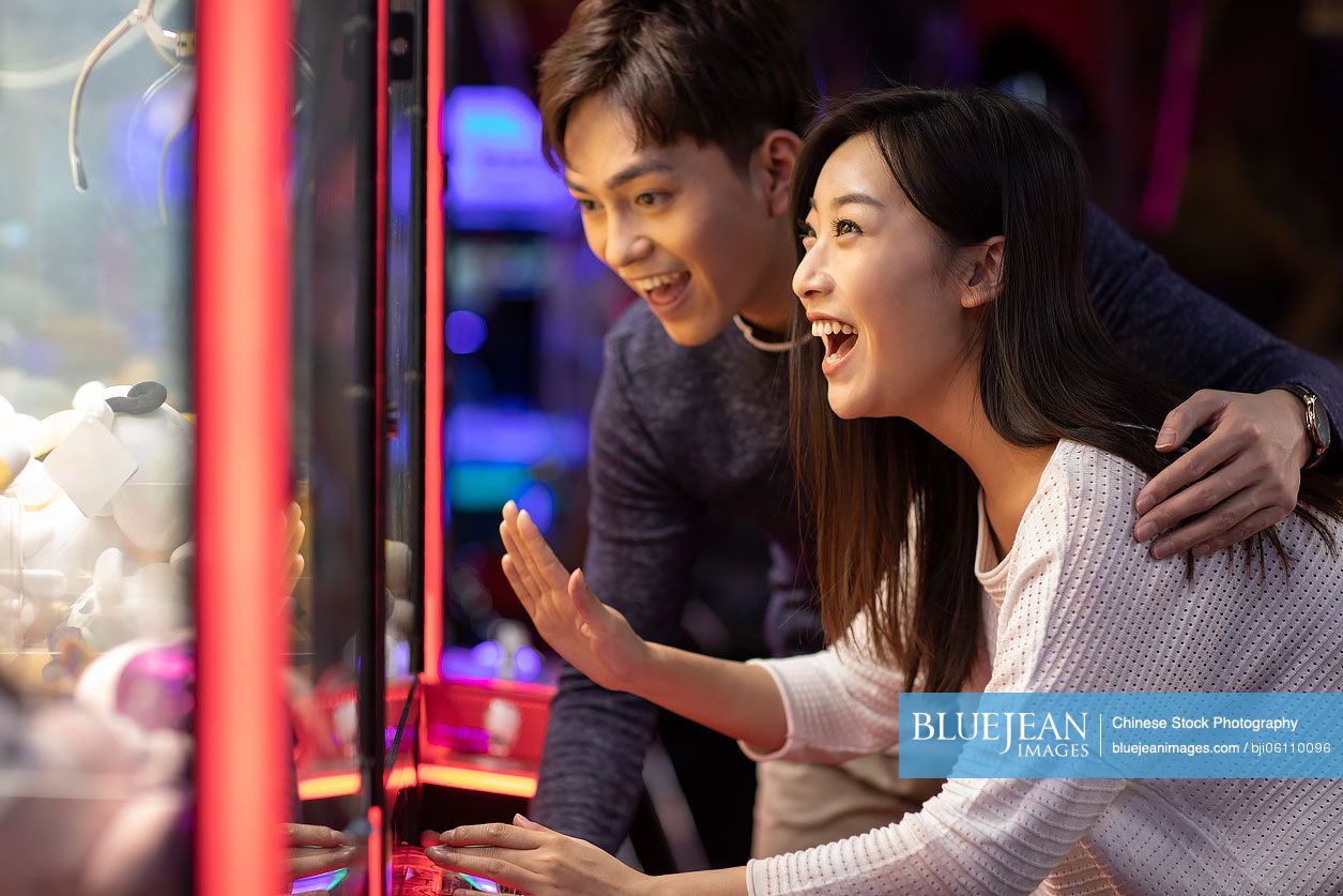 Happy young Chinese couple playing in amusement arcade