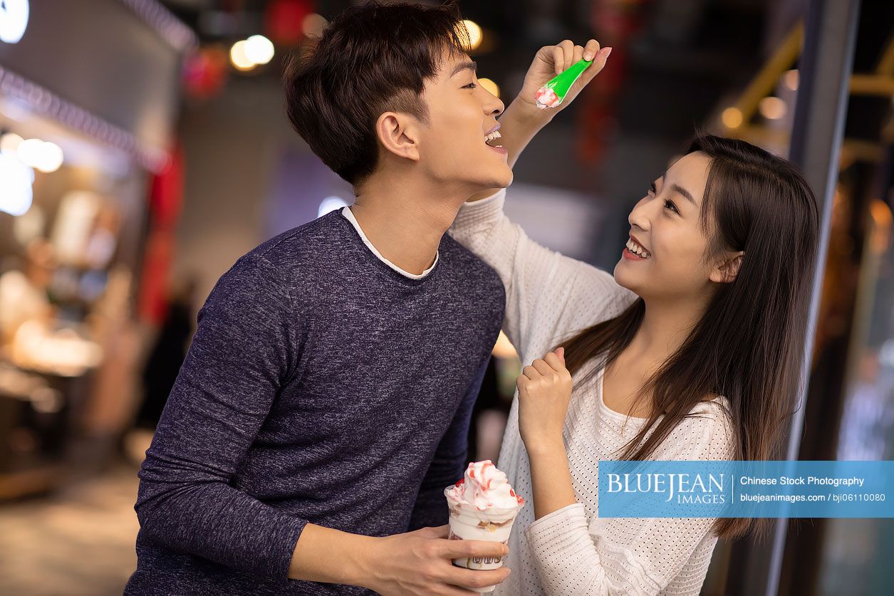 Happy young Chinese couple sharing ice cream in shopping mall