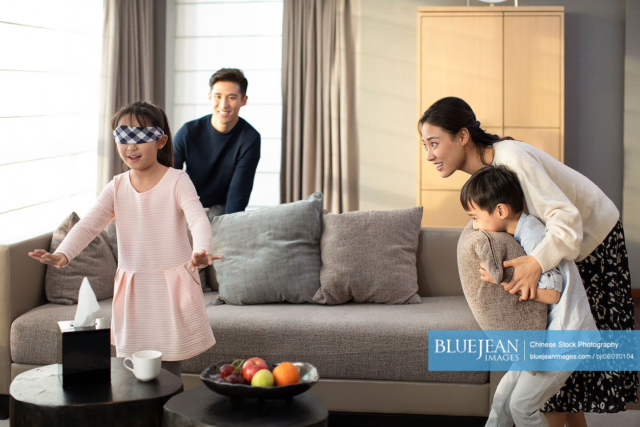 Happy young Chinese family playing hide and seek in living room