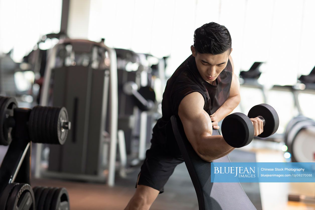 Young Chinese man working out with dumbbell at gym