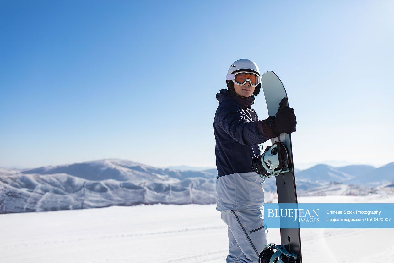 Young Chinese man with snowboard on the snow