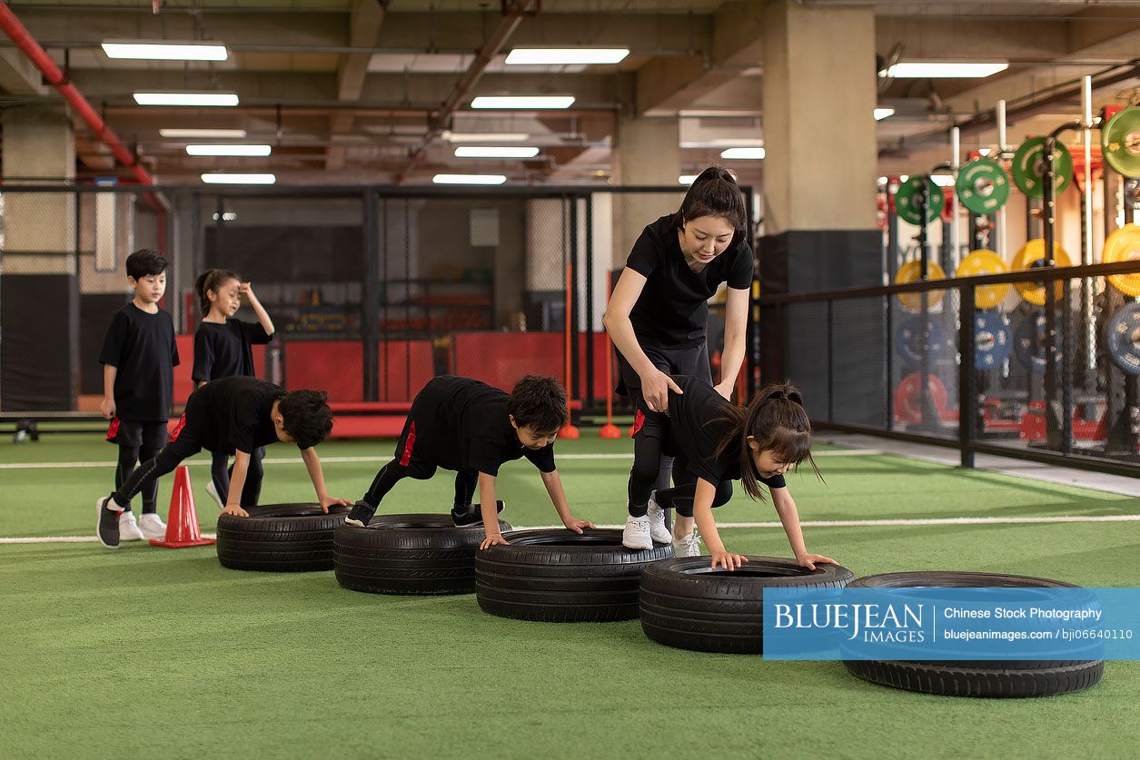 Active Chinese children having exercise class with their coach in gym