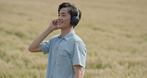 Happy young Chinese man wearing headphones in wheat field,4K