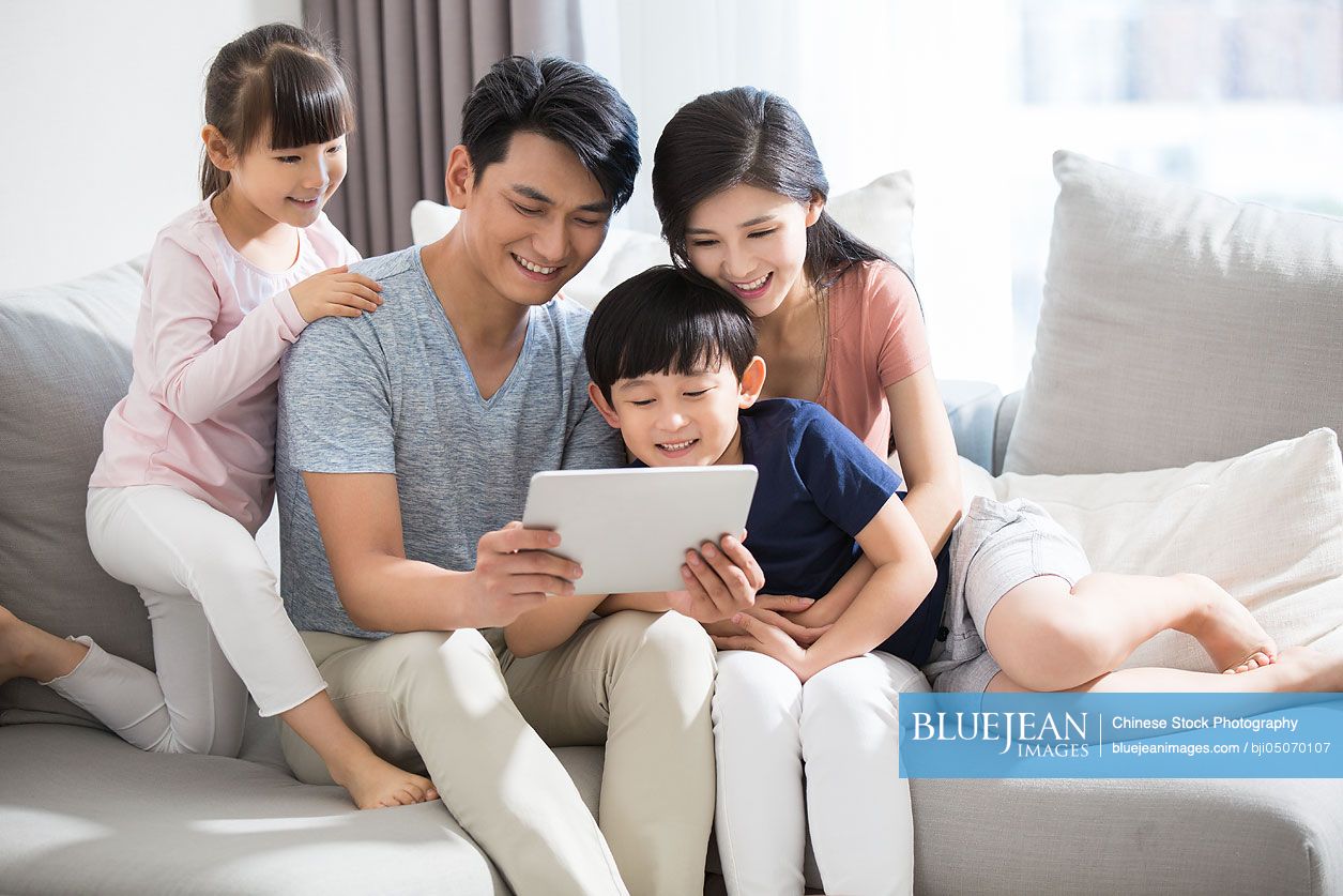 Happy young Chinese family using digital tablet at home