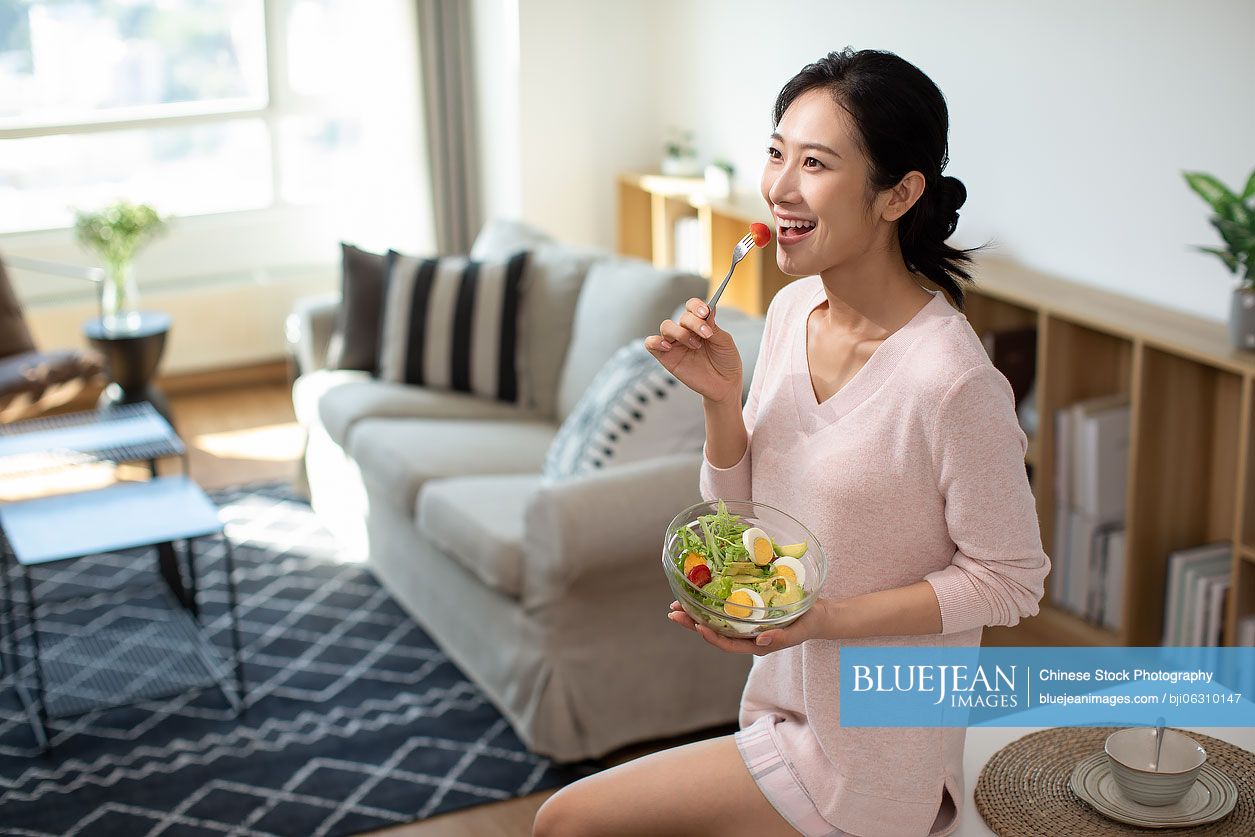 Happy young Chinese woman eating salad at home